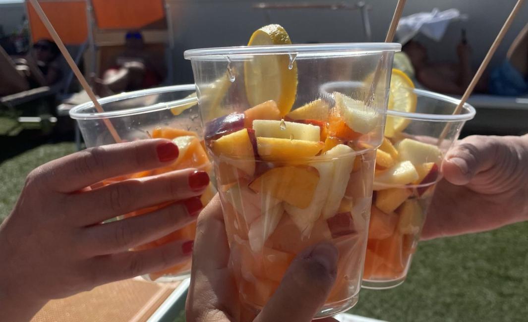 Two hands holding colorful fruit cups under the summer sun.